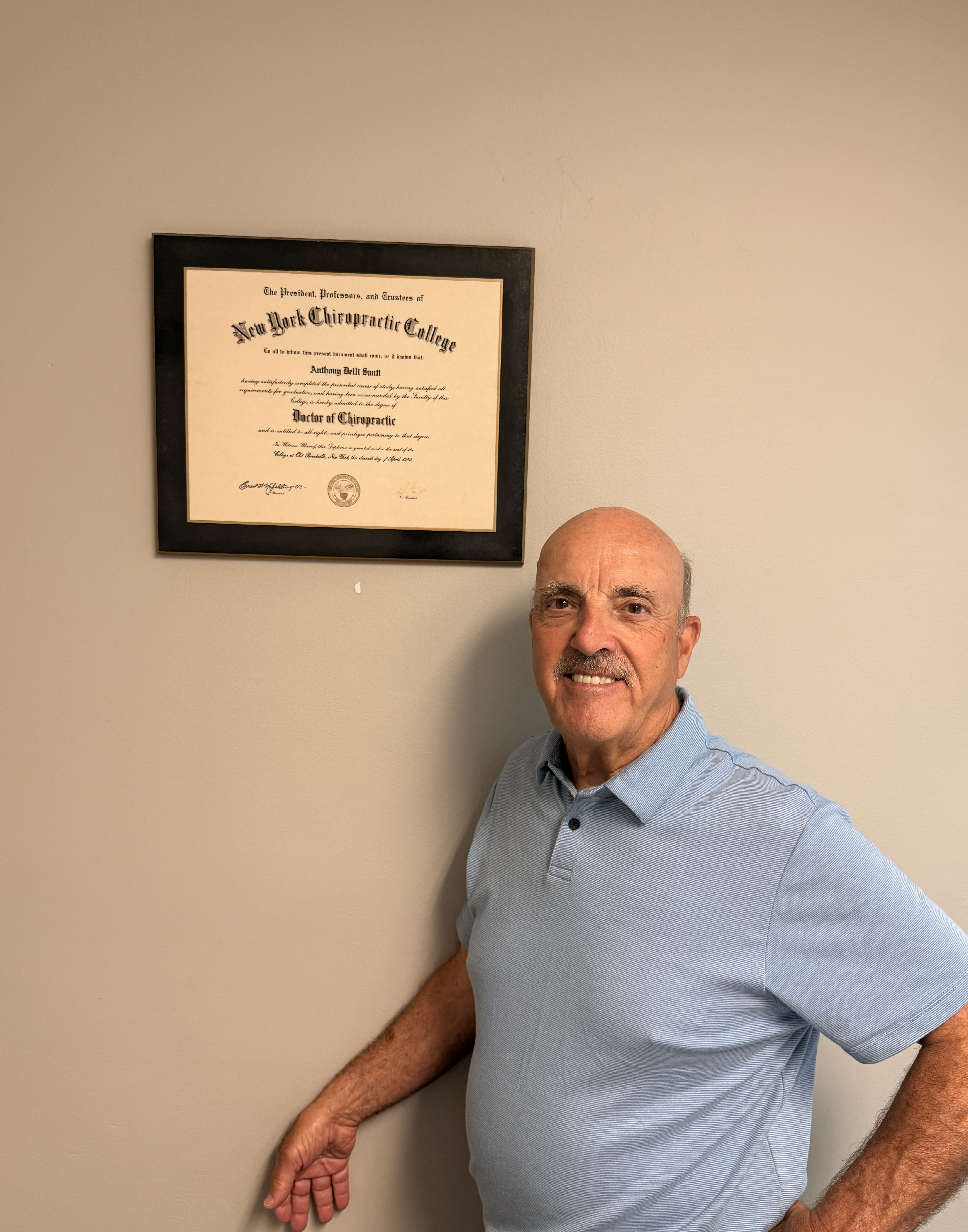 Dr. Anthony Delli Santi, DC — standing beside his New York Chiropractic College diploma